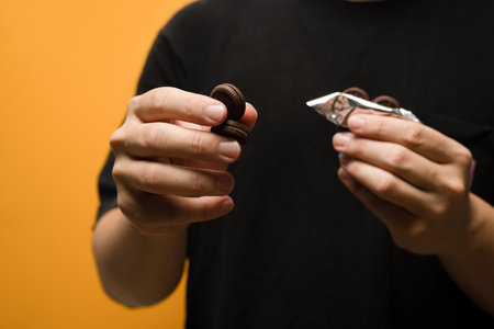 Unrecognizable man hand holding cookies with cream isolated on yellow background.の写真素材