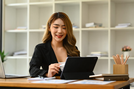 Beautiful female company worker or manager using digital tablet on wooden desk.の写真素材