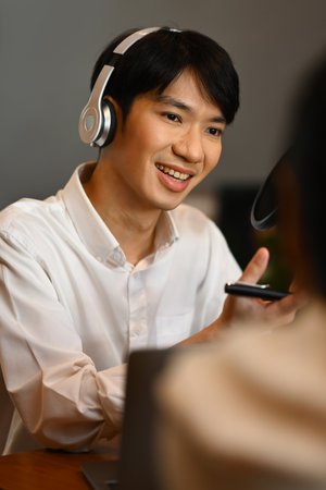 Smiling radio host wearing headphone and recording voice over radio interview guest conversation at home studio.の写真素材