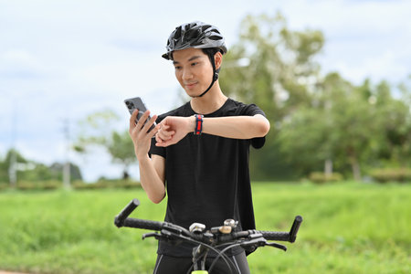 Young man taking short break after riding bicycle and checking sport activity progress data on...