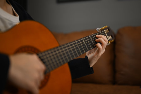 Creative hobby, entertainment and leisure concept. Unrecognizable man playing guitar on couch at home.の写真素材