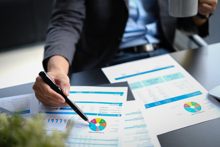 Closeup shot of professional businessman analyzing sales statistics document, using laptop at working desk.の写真素材