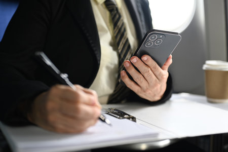 Cropped image of businesswoman in suit using smart phone while sitting comfortable seat in airplane cabin.の写真素材
