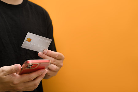 Man holding a credit card and smartphone isolated on yellow background. E-commerce, banking service, shopping online.の写真素材