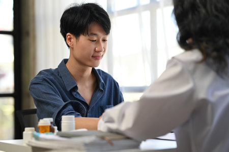 Asian man patient sitting in examining room having blood pressure checked by doctor.の写真素材