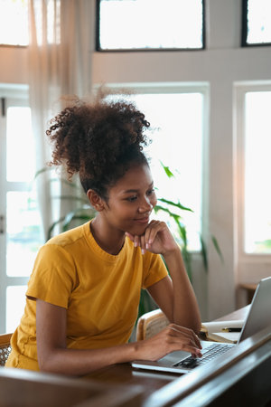 Portrait of young African American woman sitting in cozy home working remotely, surfing internet on...