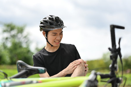 Male cyclist sitting on the ground, getting injured knee after bicycle accident.の写真素材