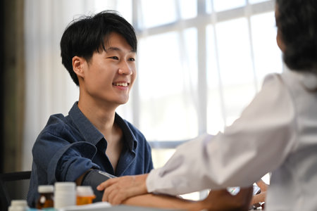 Asian man patient sitting in examining room having blood pressure checked by doctor.