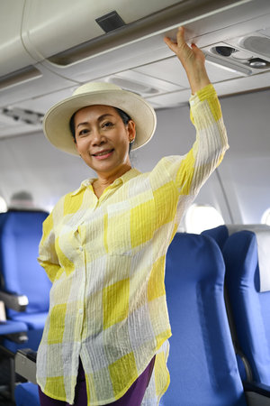 Portrait of 50s woman tourist standing at airplane aisle and smiling to camera. Retirement, travel and summer vacation concept.の写真素材