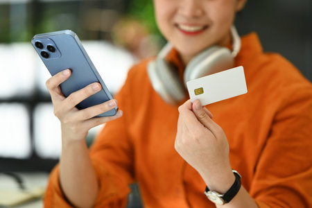 Satisfied young woman holding credit card and using smart phone, shopping on Internet or payment online.の写真素材