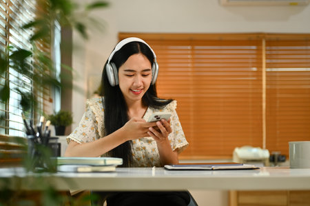 Teenage asian woman sitting at cozy home interior, chatting with friends in social media on smartphone.の写真素材