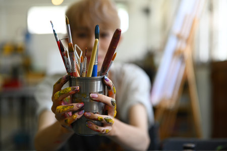 Image of male artist in apron holding metal bucket with different brushes of the artist. Art, education, creativity and people.の写真素材