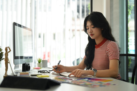 Young creative woman working with color palette, choosing color samples for design project at graphic studio.の写真素材