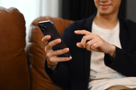 Attractive man wearing smart casual wears resting on couch and using smartphone. People and technology concept..の写真素材