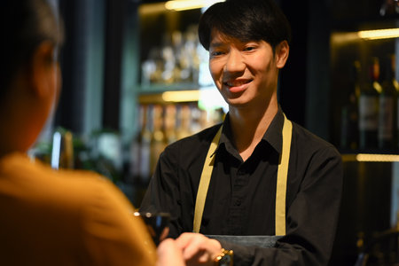 Friendly man barista wearing apron standing behind counter and serving coffee to customer. Start up, small business owner, food and drink concept..の写真素材