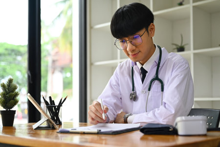 Portrait of general practitioner in white uniform sitting in modern workplace and filling medical form..の写真素材