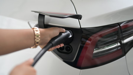 Electric car or ev is charging at station . woman use the wire power cable and plug. zero fuel no...