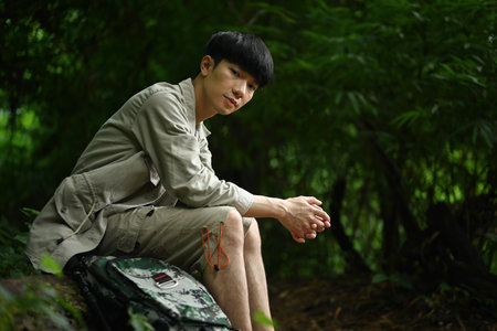 Handsome male hiker resting on top of a fallen log on the road, while exploring nature. Travel, adventure and active life concept..の写真素材