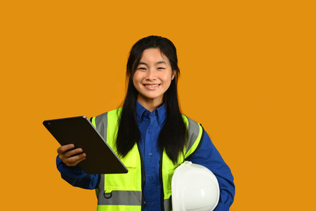 Smiling Asian girl holding helmet isolated on yellow background, future dream job career as engineer and architect.の写真素材