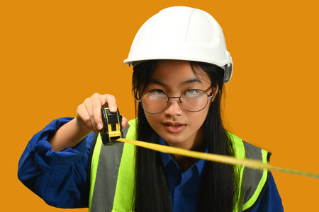 Portrait of Asian girl posing as an engineer or architect on yellow background. Dream occupation, future profession and learning concept.の写真素材