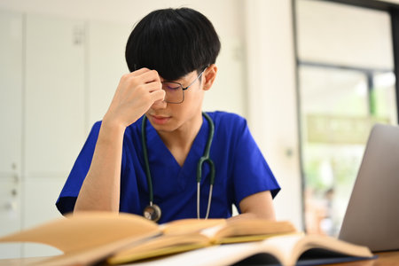 Exhausted medical student man suffering from headache or feeling tired of studying for college exam.の写真素材