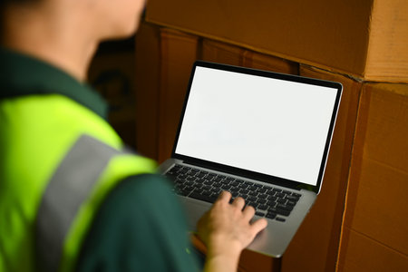 Cropped shot of warehouse worker standing between shelves with cardboard boxes and using laptop.の写真素材