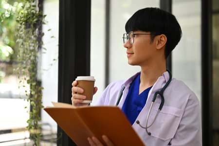 Image of general practitioner in white coat drinking coffee and looking away, thinking of future career vision.の写真素材