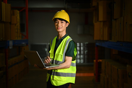 Female warehouse workers wearing hardhat holding laptop standing between retail warehouse full of shelves.の写真素材