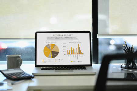 Front view laptop with graphs, charts, diagrams on screen and office supplies on white table.の写真素材