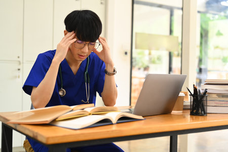 Exhausted medical student man suffering from headache or feeling tired of studying for college exam.の写真素材