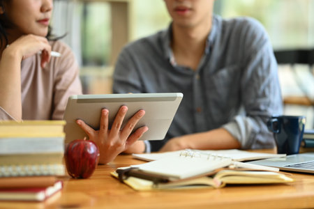 Cropped shot of college students using digital tablet, preparing for exam together in the campus.の写真素材