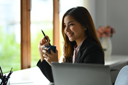 Gorgeous Asian businesswoman drinking hot coffee or tea, enjoying her leisure time during her work breakの写真素材