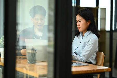 Serious female employee using laptop and preparing statistics report with her colleague in officeの写真素材