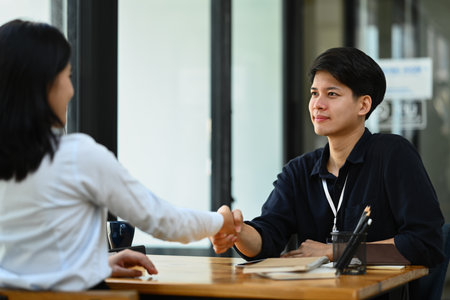 Smiling asian male manager shaking hands at briefing with coworker. Celebrate, partnership and success.の写真素材