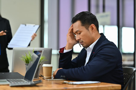 Exhausted millennial male worker feeling stressed or suffering from head ache during a meeting in the office.の写真素材