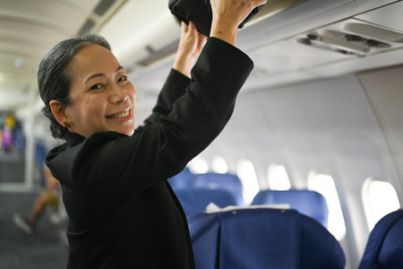 Smiling middle age woman passengers putting her luggage into the overhead compartment on an airplane.の写真素材