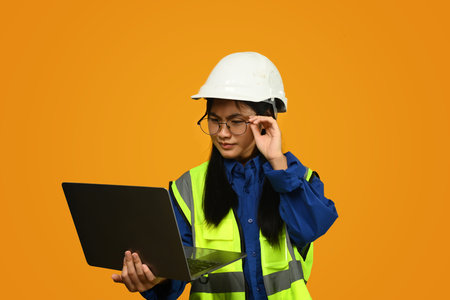Asian girl wearing helmet holding laptop isolated on yellow background, future dream job career as engineer and architect..の写真素材
