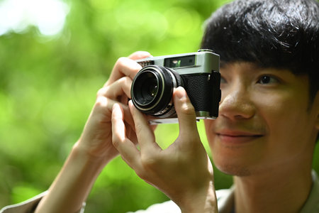 Smiling Asian male tourist with a backpack taking pictures nature landscape with camera. Travel, adventure and active life concept.の写真素材