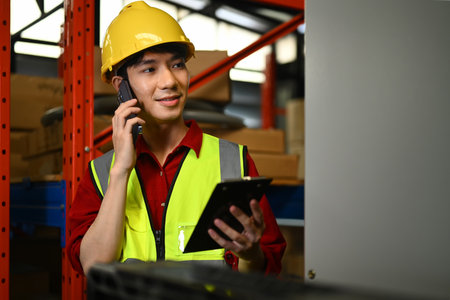 Smiling male worker talking on mobile phone while standing between retail warehouse full of shelves.