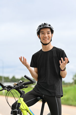 Shot of smiling male cyclist wearing wireless earphones talking on mobile phone while cycling in the park..の写真素材