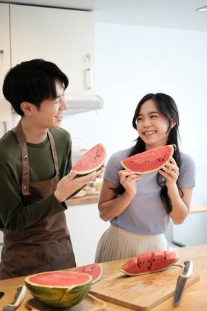 Happy asian couple eating sweet watermelon in the kitchen. Relationship and enjoying time together concept.の写真素材