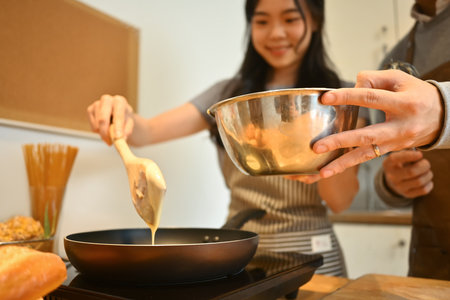Smiling young woman pouring pancake batter onto a hot electric griddle, couple preparing breakfast together.の写真素材