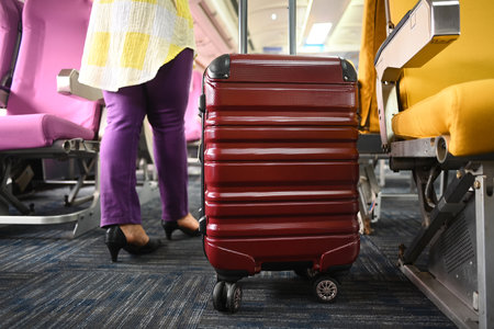 Cropped shot of 60s female tourist with suitcase walking the aisle on plane. Travel and summer vacation concept.の写真素材