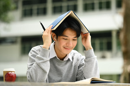 Happy asian student man putting book on his head, preparing for exam in campus. Education, Learning...