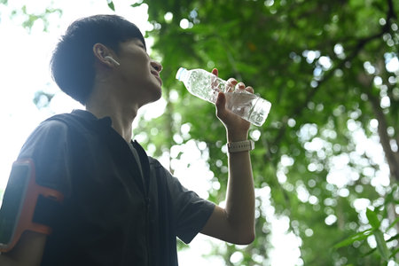 Happy asian male runner drinking water from a bottle, resting after trail running.の写真素材