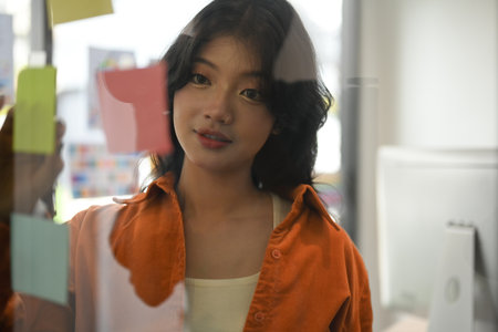 Stylish young woman reading notes on transparent board, planning goals, manage corporate work tasks.の写真素材