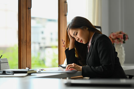 Frustrated female entrepreneur holding her hand feeling tired and stressed while sitting at office desk.の写真素材