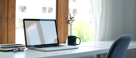 Laptop computer with white empty screen, coffee cup and book on office desk.