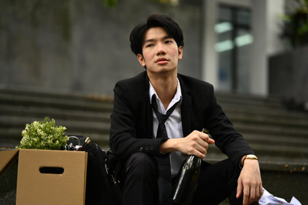 Depressed man worker drinking alcohol in front of office building after got fired. Dismissal from work, job loss, unemployment.の写真素材