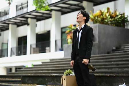 Furious man worker with beer bottle in hand yelling while standing in the office with his belongings after losing a job..の写真素材